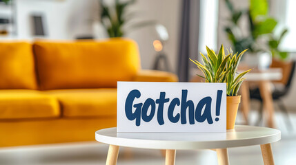 Playful april fools day greeting card Gotcha on modern living room table with yellow sofa and green plant. concept of humor, surprise, home decor, cheerful prank