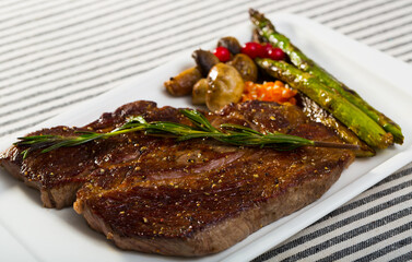 Roasted veal steak with seasonings served with baked vegetables and rosemary on striped textile surface