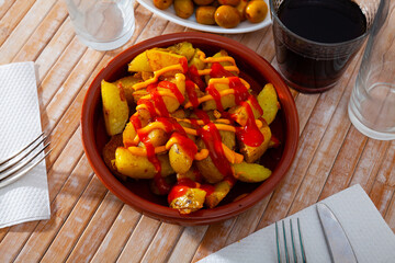 Spanish cuisine patatas bravas served with sauce on plate on wooden table