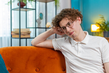 Thoughtful Caucasian man guy male sitting at home looks pensive thinks over life concerns or...