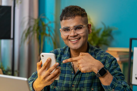 Smiling Indian man using smartphone application online pointing showing like thumbs up remote distance job working from home office. Guy freelancer recommends to use a good mobile program. Lifestyle
