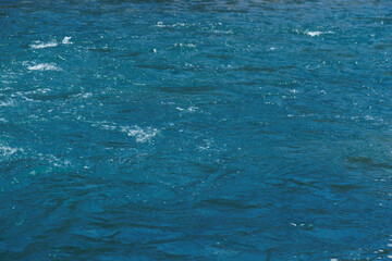 Blue water with ripples on the surface. Defocus blurred transparent blue colored clear calm water surface texture with splashes and bubbles. Water waves with shining pattern texture background.