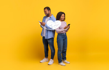 A couple stands back to back, each using their smartphone to send affectionate messages on St....