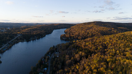 Drone view of a lake surrounded by a colorful autumn forest in Quebec, Canada, under a clear sky.