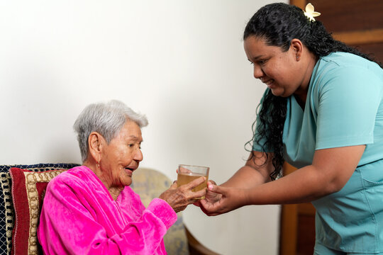 Nurse giving glass of water to elderly woman at home