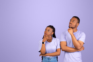Portrait of pensive African American couple thinking and looking up aside at free copy space, touching chin, standing isolated on violet studio background. Thoughtful man and woman making decision