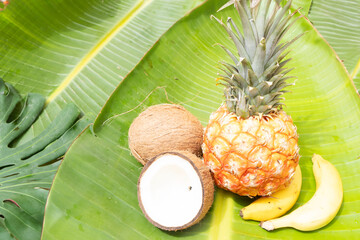 A vibrant and juicy pineapple sitting alongside a beautiful yellow flower, both resting on lush green tropical leaves
