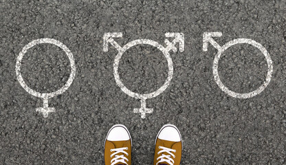 Fototapeta premium Person Standing With Transgender, Male And Female Gender Symbols Drawn On Asphalt Road. Overhead view