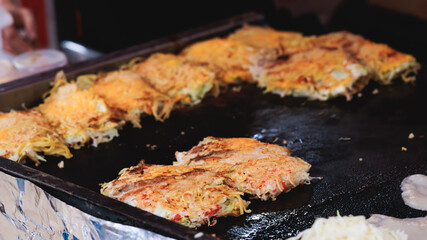 Okonomiyaki - popular Japanese Street Food, pancake with yakisoba noodles, fried egg, and pork belly, different snack selection in Kyoto, Japan, street market local vendors food stalls, teppanyaki
