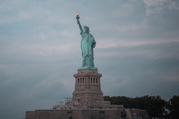 Distant view of the Statue of Liberty on Liberty Island, New York City, with a cloudy sky.