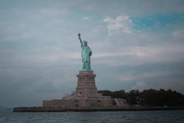 Distant view of the Statue of Liberty on Liberty Island, New York City, with a cloudy sky.