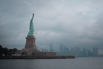 Distant view of the Statue of Liberty on Liberty Island, New York City, with a cloudy sky.