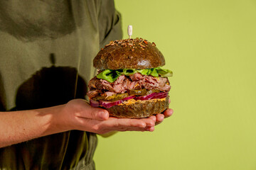 Roast Beef Sandwich, fresh lettuce, pickles, red onion, held person's hands, with green lemon...