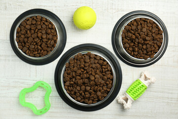 Dry pet food in feeding bowls and toys on floor, flat lay