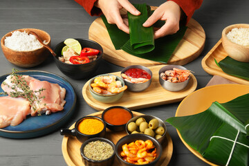 Woman wrapping food into banana leaf at wooden table with products, closeup. Healthy eco serving