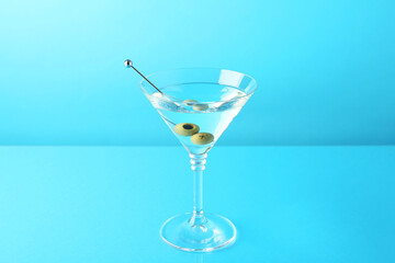 Martini cocktail with olives in glass on light blue background
