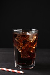 Refreshing cola with ice cubes in glass and drinking straw on black wooden table, closeup