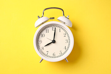 White alarm clock on yellow background, top view