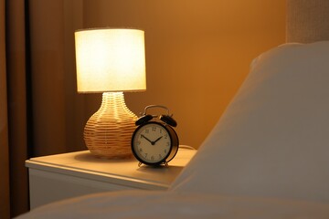 Glowing lamp and alarm clock on nightstand in bedroom