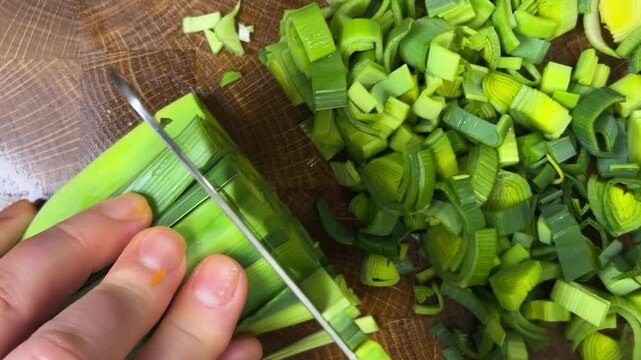 Chef chops leek stems with a cleaver on wooden cutting board.