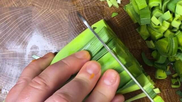 Chef chops leek stems with a cleaver on wooden cutting board.