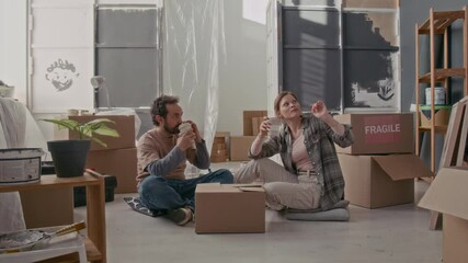 Young restful couple sitting on the floor of spacious living room of their new apartment, having coffee and discussing new creative ideas of renovation while enjoying break - Powered by Adobe