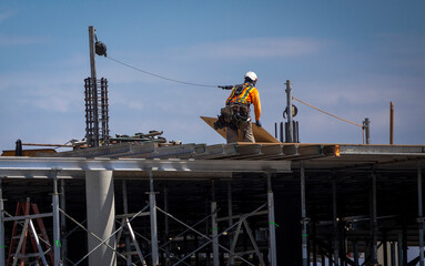 A construction woker tethered to a pole and lifting a piece of plywood