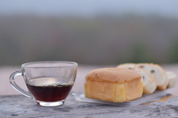 Black coffee on a wooden table with raisin bread, Bread and a glass of coffee, americano coffee cup with a mountain view background
