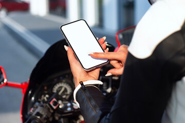 Female motorcyclist holding mockup smartphone with blank screen on the motorcycle. Concept technology on road.