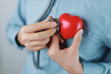 man uses a stethoscope to check the heartbeat. red heart shape exercise ball in hands with doctor...