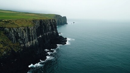 A misty coastline with rugged cliffs meets the calm sea, showcasing a serene landscape that evokes tranquility and natural beauty.