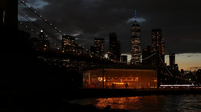Brooklyn Bridge, New York City Manhattan downtown skyline cityscape, United States. Waterfront Pebble Beach, carousel in Dumbo, USA. Dramatic twilight dusk. Evening or night sky. World Trade Center.