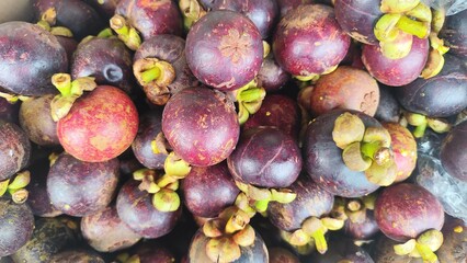 Close-up of a bunch of fresh mangosteens, showing their bright purple skin and green caps. Close-Up of fresh mangosteen background texture material.is a display in supermarket