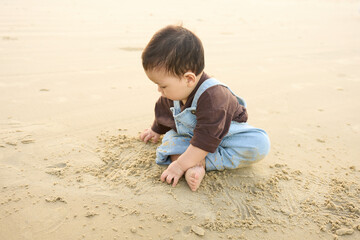 arafed baby boy sitting on the sand playing with sand
