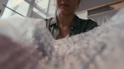 Young woman taking piece of bubble wrap while sitting on the floor of living room in new apartment during renovation and preparing fragile household items for packing - Powered by Adobe