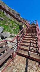 A wooden staircase ascends towards a cliffside walkway against a backdrop of a clear blue sky. the...