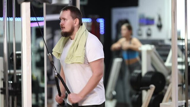Bearded man in gym performs strength exercises for arm muscles using cable crossover machine. Athlete works out at gym and pumps muscles of arms and upper torso. 