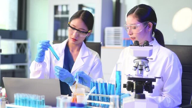 Two Asian female scientists in a high-tech lab analyzing biochemical samples, using micro pipettes,