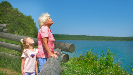 Grandmother and granddaughter stand together hugging and enjoy by the lake or sea. Summer vacation...