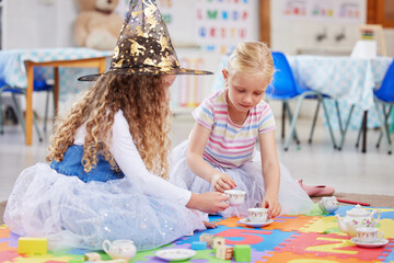 Girl, friends and tea party with play in classroom for witch costume, hat or learning on floor. Children, magic and help for social development, growth or game with toys, fun or cups at kindergarten © peopleimages.com