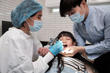 Obraz premium Asian female pediatric dentist examines a girl's teeth in dental clinic and takes care and encourages of father, mouth oral hygiene, and professional orthodontic healthcare work in a kid hospital.