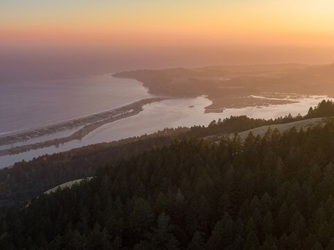 Coastal sunset overBolinas Lagoon with a dense forest fof Mt Tam on the hillside. Golden hour light bathes the scene. Stinson Beach, San Francisco, California, USA