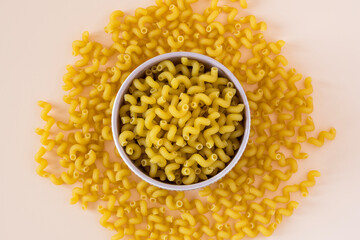 Top  view of a porcelain bowl of raw italian durum wheat cavatappi pasta against a light ochre...