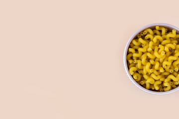 Top  view of a porcelain bowl of raw italian durum wheat cavatappi pasta against a light ochre...