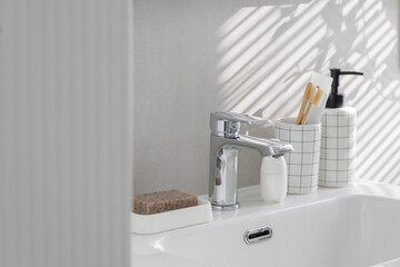 Clean white stylish washbasin with faucet, liquid soap, wooden toothbrushes and cosmetics.