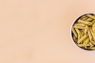 Top view of a bowl of raw italian durum wheat penne lisce pasta against a light ochre background ....