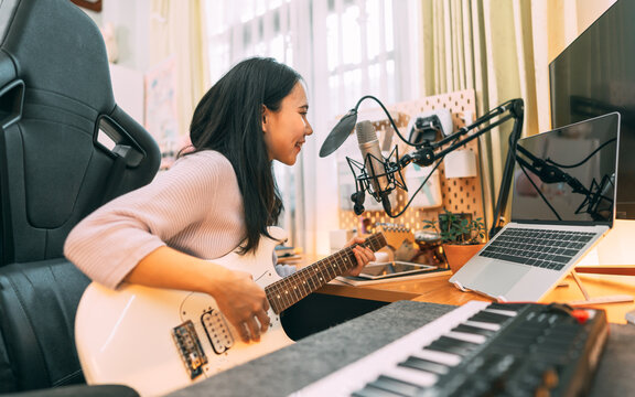 Young asian woman composer playing guitar music with digital technology at home studio