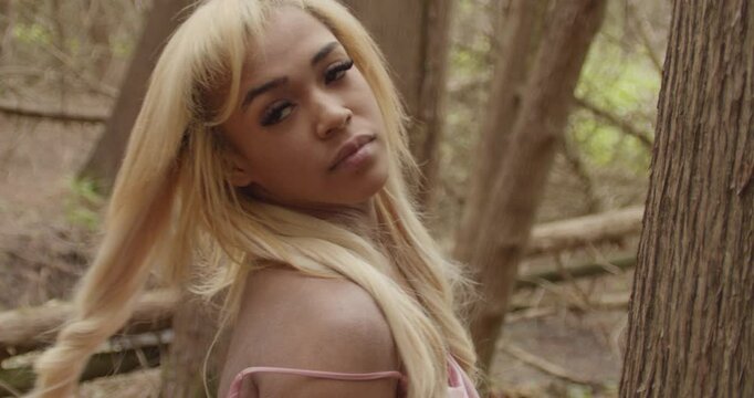 Young ebony woman in pink gown. Handheld camera in close up tilts from her hands to her face . She flips her hair before looking seductively at camera. She looks upward to the sky. 60fps slow motion.
