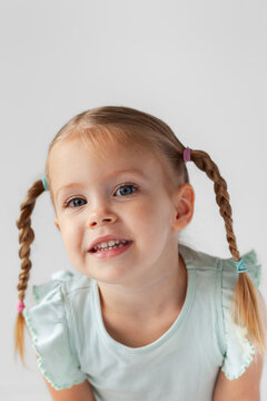 Portrait of little girl on white with plaited pigtails