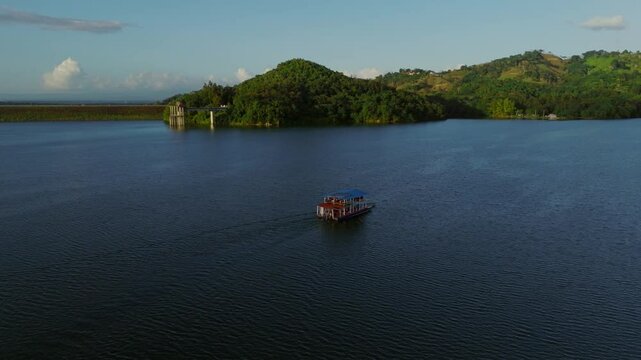 Ferry cruising on Hatillo Dam reservoir at sunset, Dominican Republic. Aerial drone orbiting, copy space